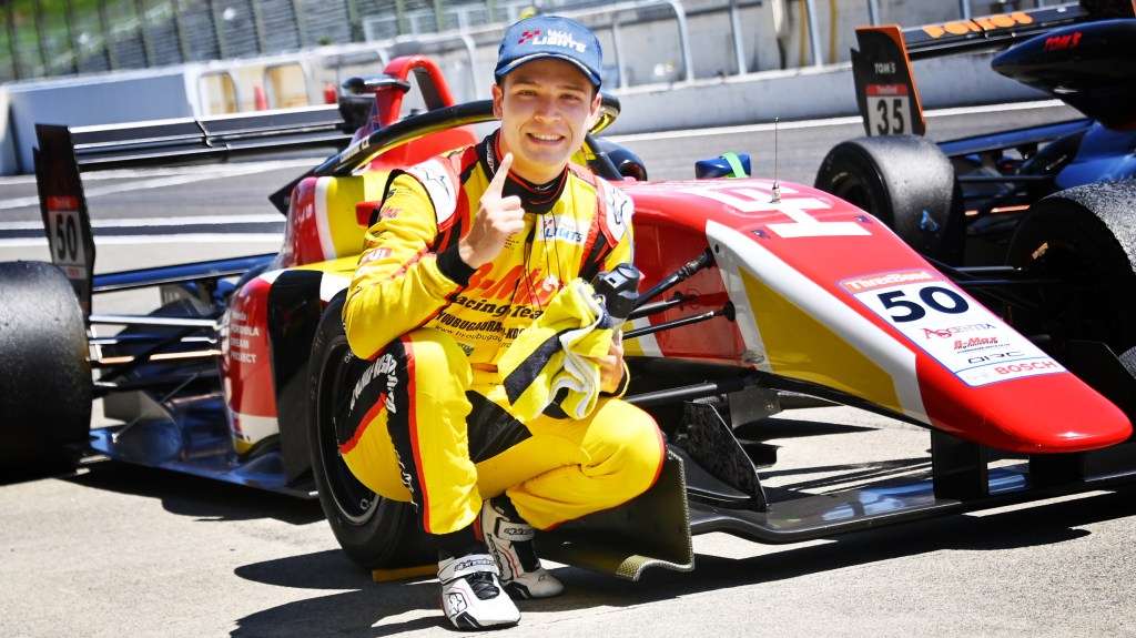Kimura in front of his car pointing his finger in the air